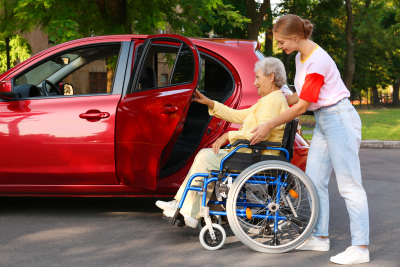 young woman helping a senior on a wheelchair get on a car